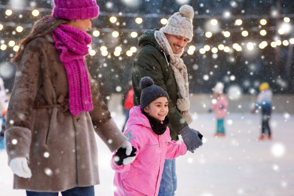 christmas, family and leisure concept - happy mother, father and daughter at outdoor skating rink in winter over snow