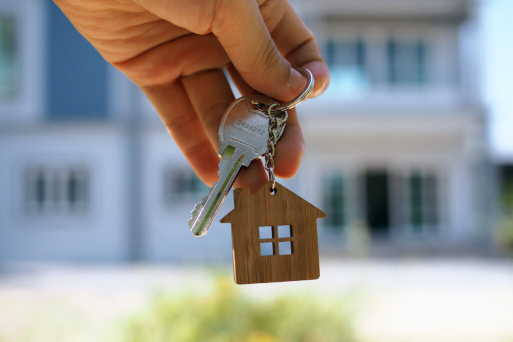 A hand holding new house keys with a wooden keychain after your offer is accepted on a new home.