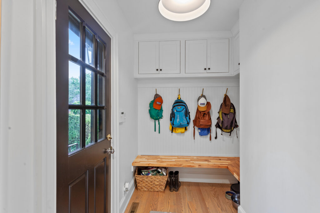 A clean entryway mudroom with backpacks hanging on hooks and a wood bench evaluating if your home is working for you.