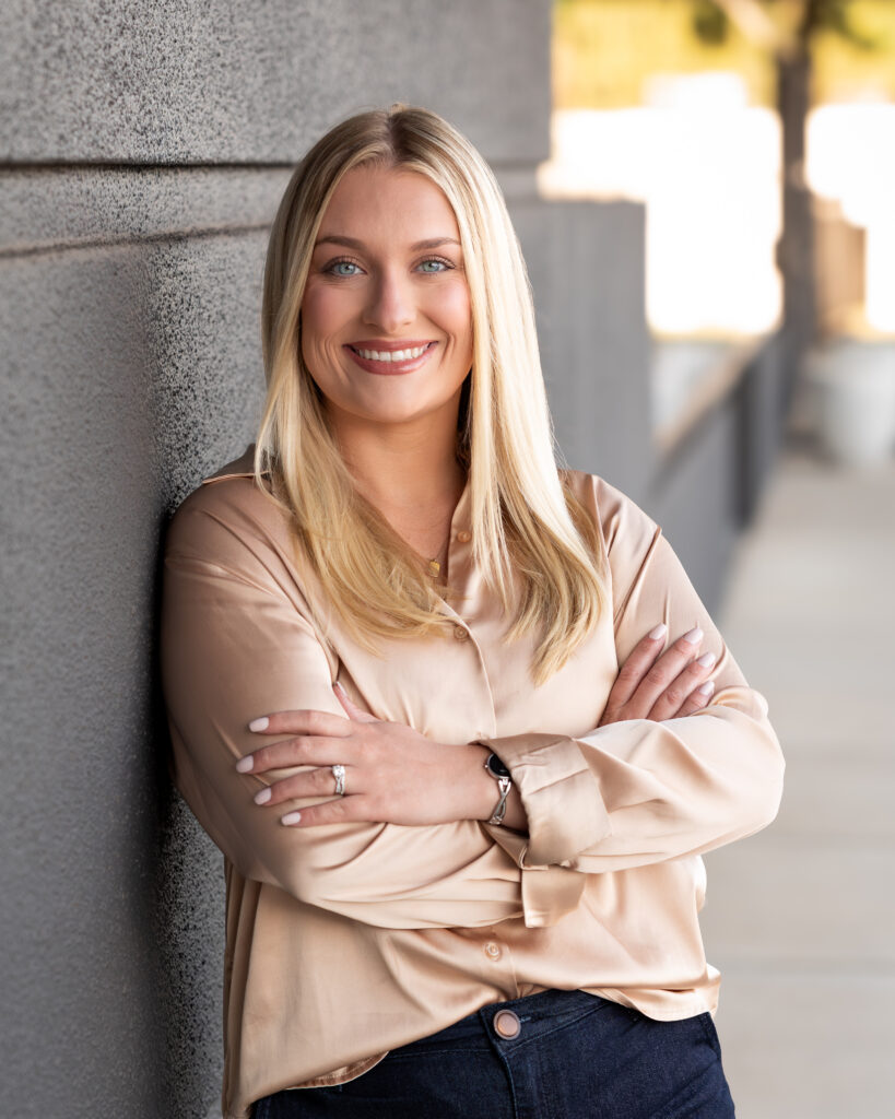 Professional headshot of REALTOR® Kayla Guin smiling in a champagne-colored blouse against a dark textured background.