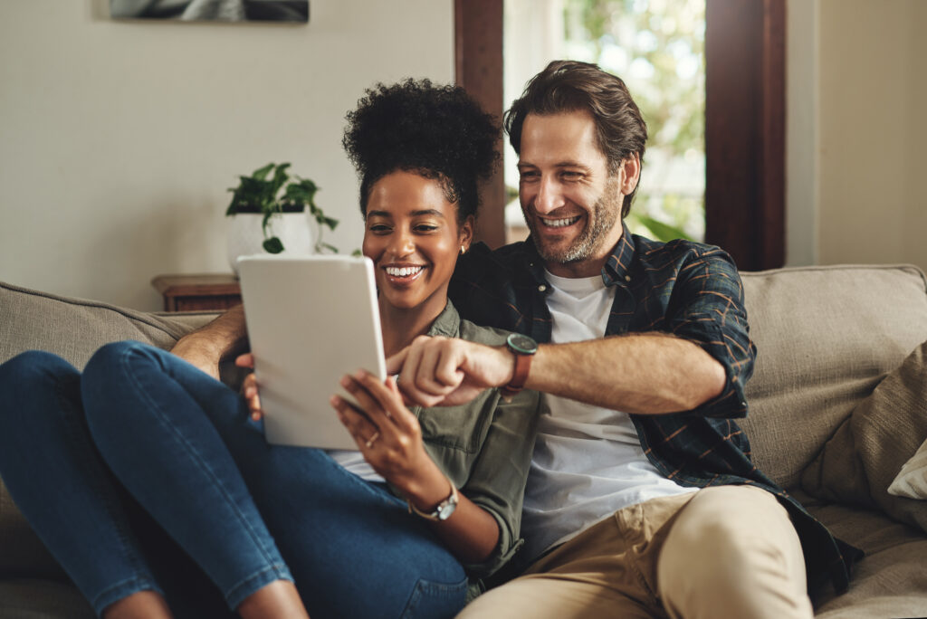 A smiling couple sitting on a couch using a tablet to calculate mortgage rate buydown savings and home loan affordability in Upstate South Carolina.